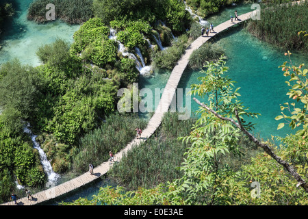 Touristen zu Fuß auf einem hölzernen Fußweg über kristallklares Wassersee im Nationalpark Plitvicer Seen in Kroatien. Stockfoto