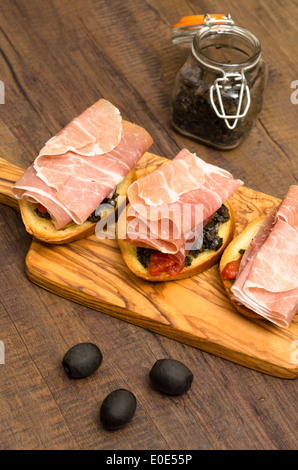 Snack mit Rohschinken und schwarzen Oliven-Paste auf Weißbrot in Hochformat Stockfoto