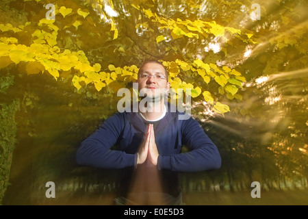 Lässig gekleidet jungen Mann, Blick in die Kamera mit Namaste Gruß im Herbst Park. Stockfoto