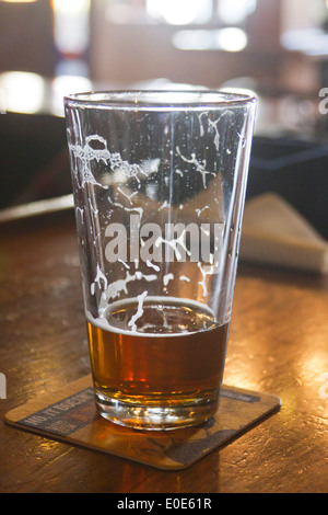 Nahaufnahme von einem meist betrunken Glas Bier mit Trocknung Schaum auf eine Achterbahn an der Bar sitzen Stockfoto