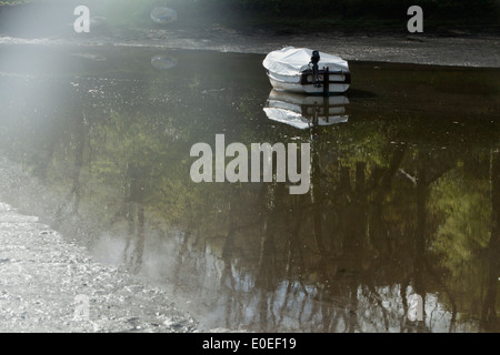 Ein nebliger Morgen an der Cornish Dorf while bei Ebbe am Fluss Gezeiten mit der Spiegelung im Wasser eines Bootes. Stockfoto