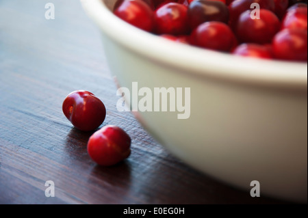 Zwei Kirschen liegen neben einer Schüssel voller Kirschen Stockfoto