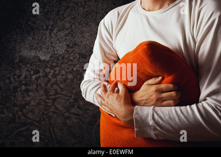 Mann umarmt orange Kissen im dunklen Raum. Konzept von Kummer, Traurigkeit und Depression. Stockfoto