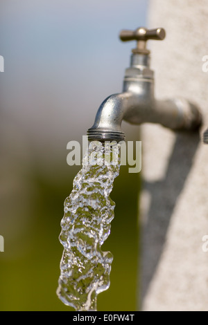 Wasser fließt aus Wasserhahn im Freien an einem sonnigen Tag. Stockfoto