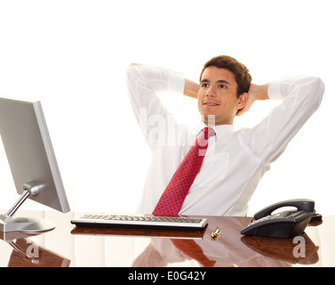 Ein erfolgreicher junger Manager sitzt mit Schreibtisch und lächelt., Ein Erfolgreicher Junger Manager Sitzt Bei Schreibtisch Und Laechelt. Stockfoto