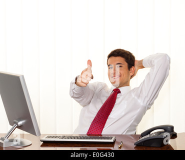 Ein erfolgreicher junger Manager sitzt mit Schreibtisch und lächelt., Ein Erfolgreicher Junger Manager Sitzt Bei Schreibtisch Und Laechelt. Stockfoto