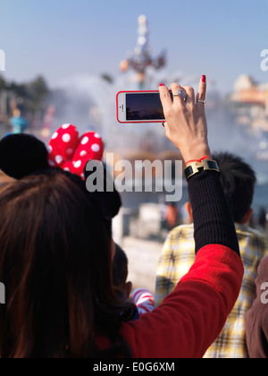 Frau, die Aufzeichnung einer Sendung mit ihrem iPhone im Tokyo Disneysea Themenpark. Japan. Stockfoto