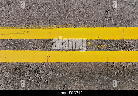 Doppelte gelbe Linien horizontal verlaufende auf asphaltierter Strasse. Stockfoto