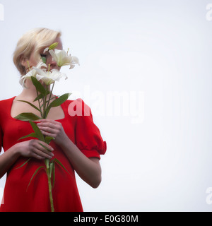 eine Frau in einem roten Kleid versteckt ihr Gesicht hinter weißen Lilien