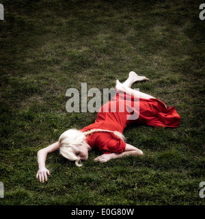 eine Frau in einem roten Kleid ist in der Wiese liegen. Stockfoto