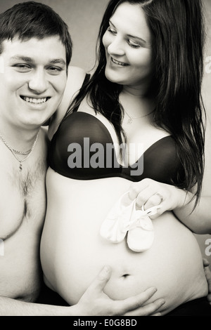 Schwangere Frau mit einem Kind den Schuh, ihr Mann zärtlich hält ihren Bauch, schwarz / weiß Stockfoto