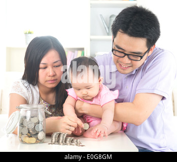 Asiatisches Baby, Münzen in der Glasflasche mit Hilfe der Eltern. Geld sparen Bildungskonzept. Stockfoto
