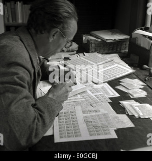 1950er und eine historische Bild zeigt einen Mann an einem Schreibtisch mit Zigarette, die Überprüfung der Qualität der Blätter von Briefmarken. Stockfoto