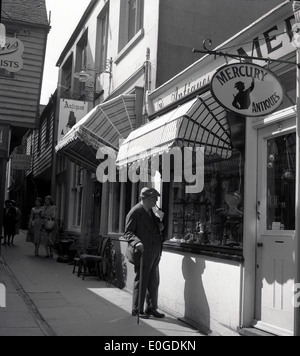 1950er Jahre historische Bild, Seitenstraße, Brighton, ein älterer Mann mit Stock schaut die Schaufenster von Quecksilber Antiquitäten. Stockfoto