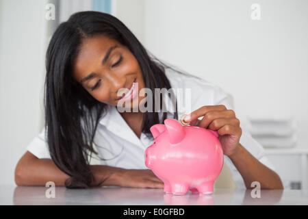 Lächeln, Geschäftsfrau, Münzen in die Piggy Bank an ihrem Schreibtisch Stockfoto