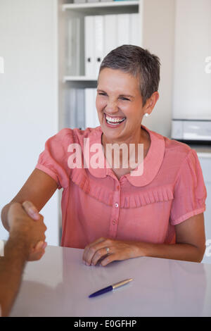 Lachend Geschäftsfrau Händeschütteln am Schreibtisch Stockfoto