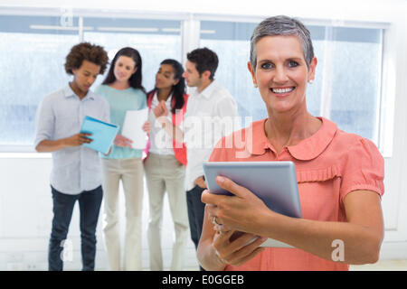 Geschäftsfrau lächelt in die Kamera beim Betrachten der Tablet-pc mit Kollegen hinter ihr Stockfoto