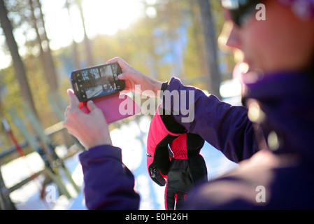 Junge attraktive Frau nehmen Foto mit Handy im Skigebiet Pyhä, Lappland Stockfoto