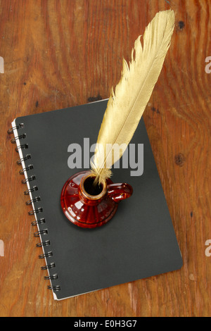 Goldene Feder im Tintenfaß auf einem schwarzen Tagebuch Stockfoto