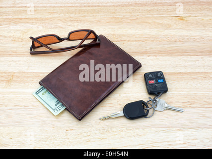 Eine Reihe von Autoschlüsseln mit Sonnenbrille auf einer hölzernen Tischplatte ein Leder-Portemonnaie mit Bargeld. Stockfoto