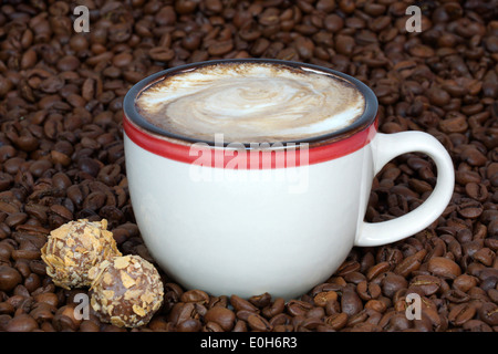 Tasse Kaffee und Süßigkeiten auf Kaffeebohnen Hintergrund Stockfoto