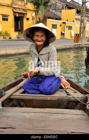 Ältere, lächelnde Vietnamesin, die Touristen für Fahrten auf dem Fluss in der Stadt Hoi an, Vietnam, nimmt und vom Heck ihres Flussboots paddelt. Stockfoto