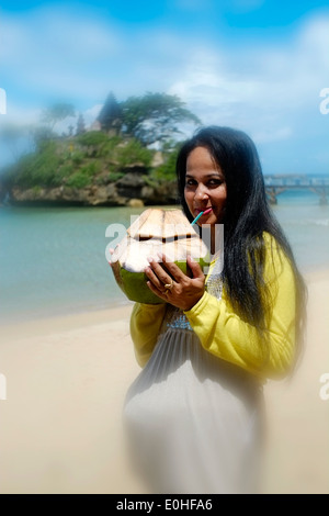 Schwangere Frau trinken aus frischen Kokosnuss am Strand am Meer im Balekambang Ost-Java-Indonesien Stockfoto