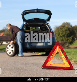 Radwechsel auf eine kaputte Auto auf einer Straße mit roten Warndreieck Stockfoto