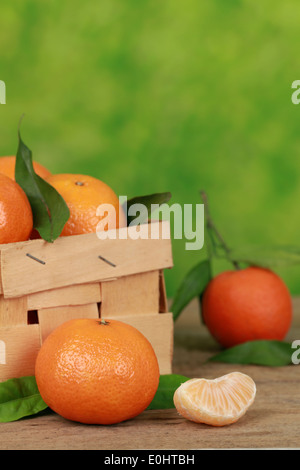 Mandarinen in einer Holzkiste auf einem Tisch mit grünem Hintergrund und Exemplar Stockfoto