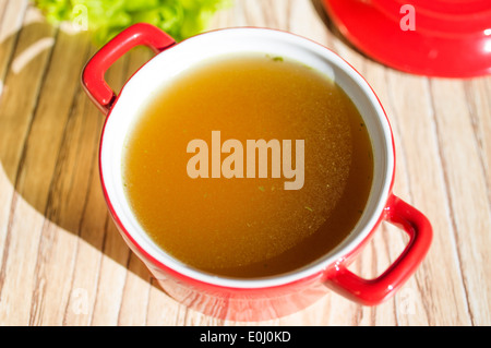 Hühnerbrühe, Bouillon, klare Suppe in der Tasse neben frischen Kräutern. Stockfoto