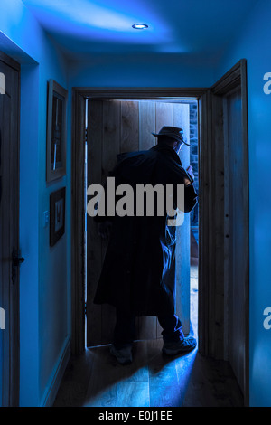 Ein Mann mit einem Hut und langen Regenmantel, die einen Raum betreten. Stockfoto