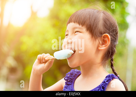 glückliche kleine Mädchen essen Eis am Stiel im Sommer mit Sonnenuntergang Stockfoto