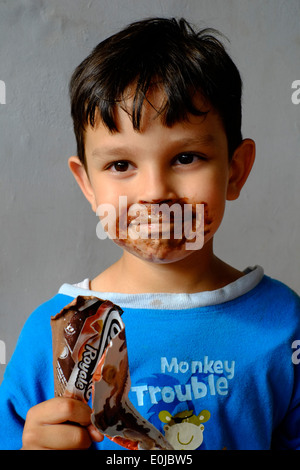 kleiner Junge ein Schokoladeneis zu essen und immer das meiste davon über sein Gesicht verschmiert Stockfoto