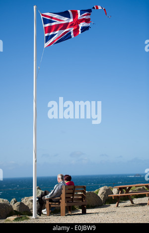 Ein paar sitzen unter einem Union Jack-Flagge bei Lands End in Cornwall, England. Stockfoto