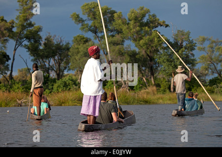 Poler mit Touristen auf ihrem traditionellen Mokoro-Boot in das Okavango Delta, Botswana, Afrika Stockfoto