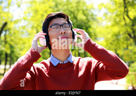 Junge asiatische Mann anhören von Musik im park Stockfoto