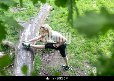 Blonde Dame tragen schwarze Leggings und eine graue Ernte erstreckt sich ihr Bein auf einem Baumstamm in Hampstead Heide. Stockfoto