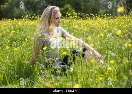 Blonde Dame tragen schwarze Leggings und ein grauer Crop Top sitzen in langen Rasen mit gelben Blüten Hampstead Heath. Stockfoto