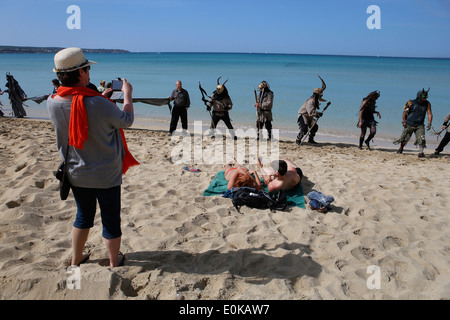 Touristen am Strand Sonnenbaden zu reagieren, wie Aktivisten in schwarz und als Teufel Protest gegen Öl Prospektionen im Bereich gekleidet Stockfoto