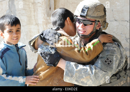 US Armee Sgt. Joshua Vicenzi stoppt, um einem irakische Kind eine Umarmung während er zusammen mit US-Soldaten von der 1. Combat Arms Bat Stockfoto