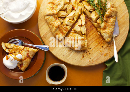 Eine Draufsicht einer Portion Apfel Galette mit Schlagsahne und Ahornsirup, neben sitzt die ganze frische gebackene Galette. Stockfoto