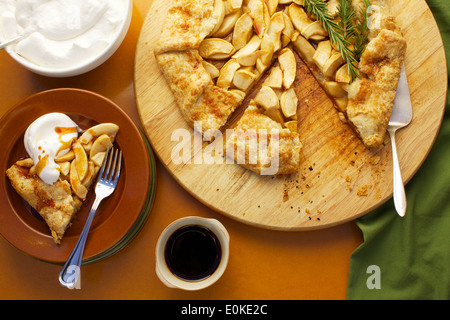 Eine Draufsicht einer Portion Apfel Galette mit Schlagsahne und Ahornsirup, neben sitzt die ganze frische gebackene Galette. Stockfoto