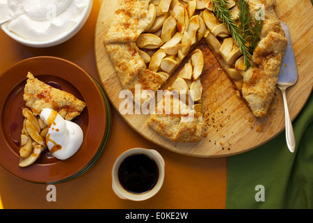 Eine Draufsicht einer Portion Apfel Galette mit Schlagsahne und Ahornsirup, neben sitzt die ganze frische gebackene Galette. Stockfoto