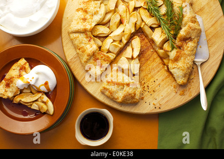 Eine Draufsicht einer Portion Apfel Galette mit Schlagsahne und Ahornsirup, neben sitzt die ganze frische gebackene Galette. Stockfoto