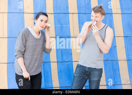 Junger Mann in einer Blechdose Telefon und Frau hören sprechen. Konzeptbild von Kommunikation und hören in einer Beziehung. Stockfoto