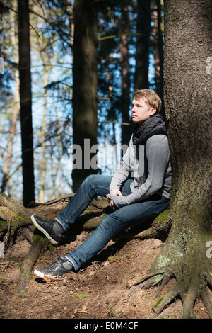 Nachdenkliche Jüngling in der Natur durch einen Baum im Wald während einer Wanderung ausruhen. Stockfoto