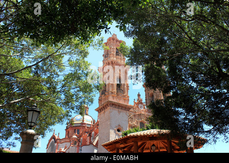 Der Glockenturm und gekachelten Kuppel der Kirche von Santa Prisca, gesehen durch die schattigen Bäume im Plaza Borda, Taxco, Mexiko Stockfoto