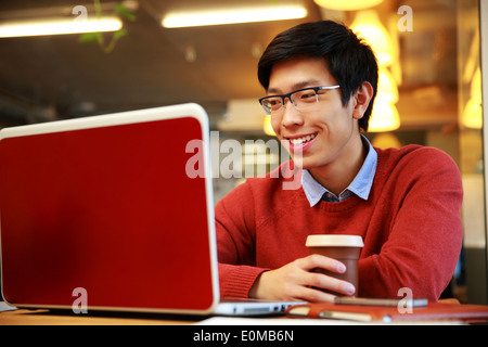 Asiatische glücklich in Gläsern am Laptop arbeiten und halten Tasse Kaffee Stockfoto