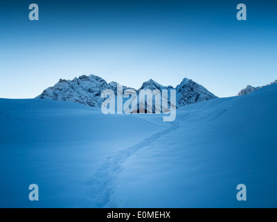 Ein Pfad führt durch den frischen Schnee in den Schweizer Alpen, in den frühen Morgenstunden Stockfoto