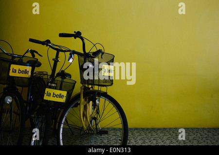 Drei Fahrräder mit Körben zur Miete vor einer gelben Wand. Stockfoto